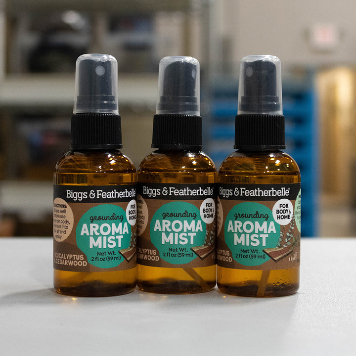 Three amber spray bottles of Biggs &amp; Featherbell Grounding Aroma Mist lined up on a light surface with a blurred indoor background.