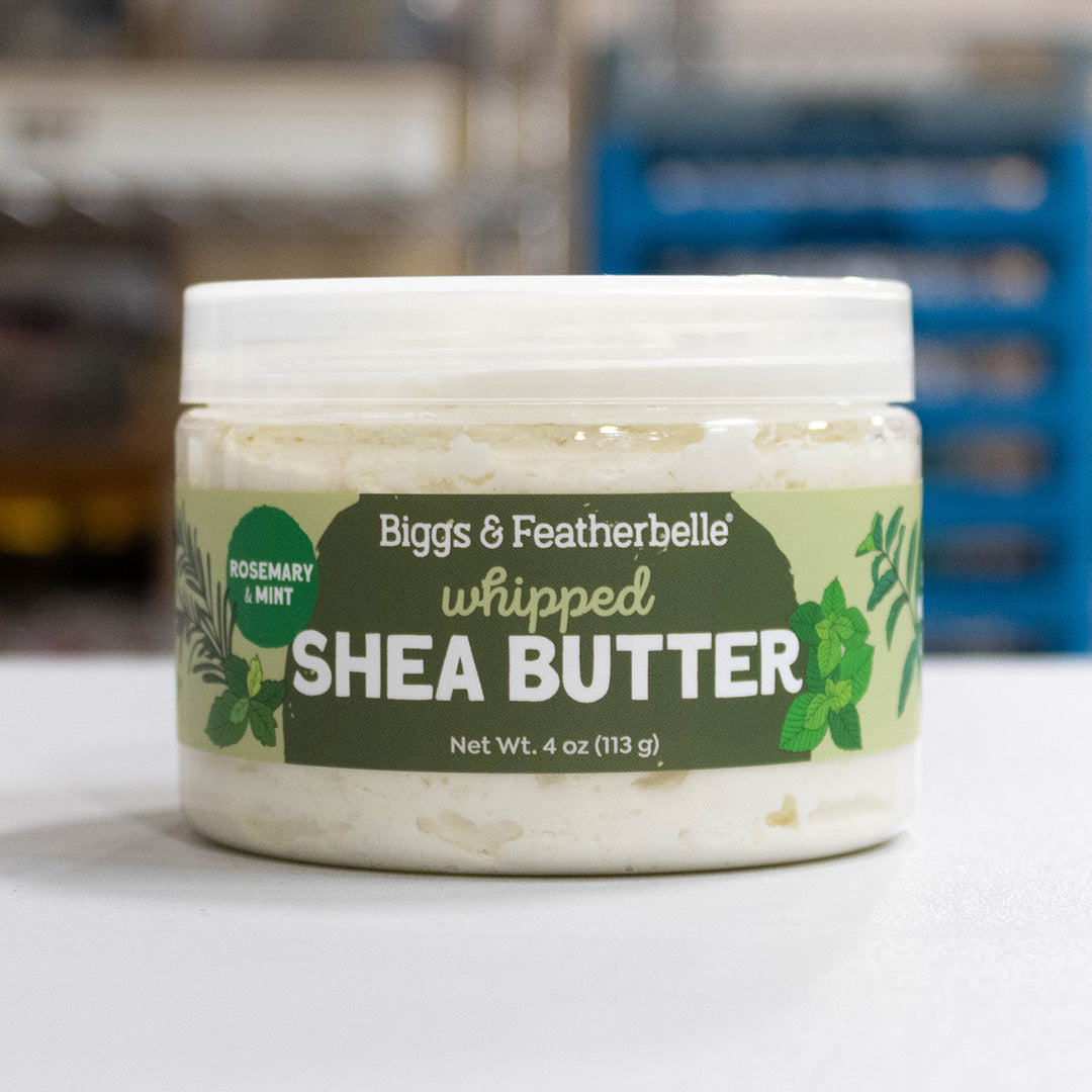 A jar of Biggs &amp; Featherbelle whipped Shea Butter in Rosemary &amp; Mint scent, shown on a light surface with a blurred background.