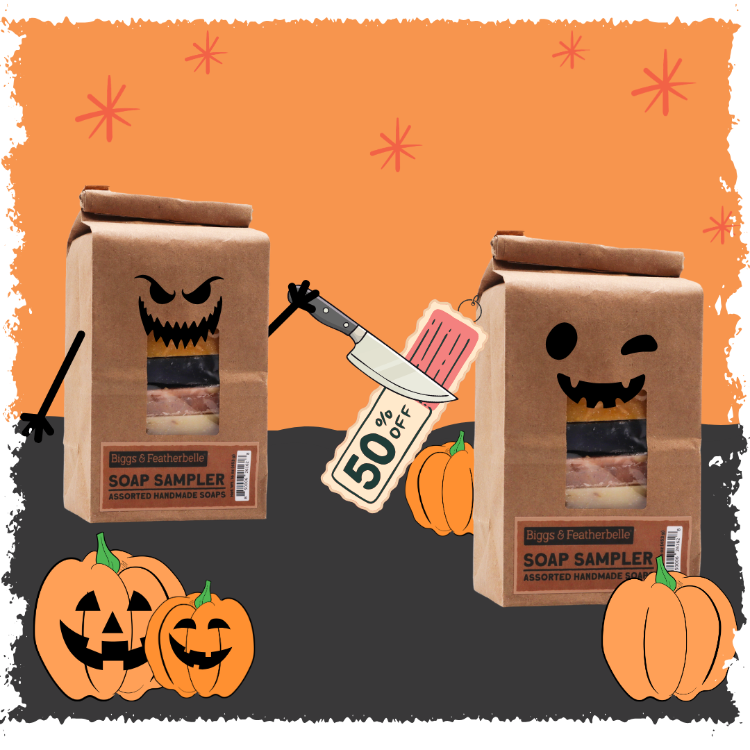 Two brown paper soap sampler bags with Halloween faces are shown on a dark gray surface against an orange background. One bag has a knife and a 50% off tag, while the other shows a wrapped bar of soap.