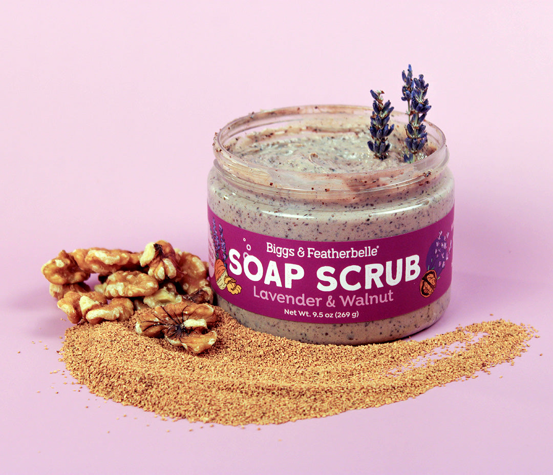 Jar of Lavender & Walnut Soap Scrub with lavender and walnut on a pink background