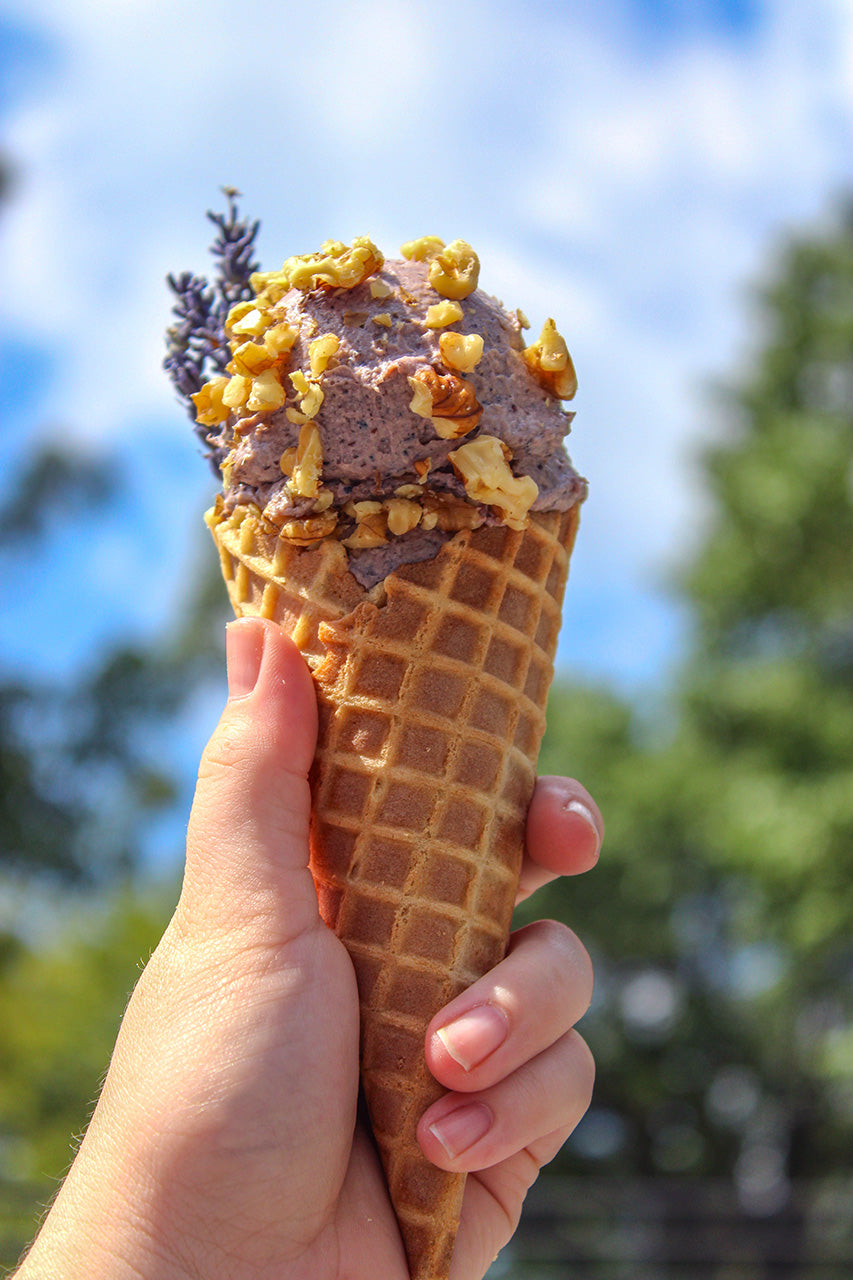 Hand holding a waffle cone with Lavender & Walnut Soap Scrub topped with walnuts against a blurred natural background